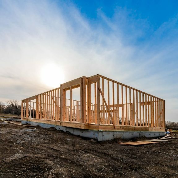 The structure of wood framing at construction site against a vast cloudy sky with bright sun behind.
